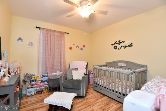 bedroom featuring a nursery area, ceiling fan, and light hardwood / wood-style flooring