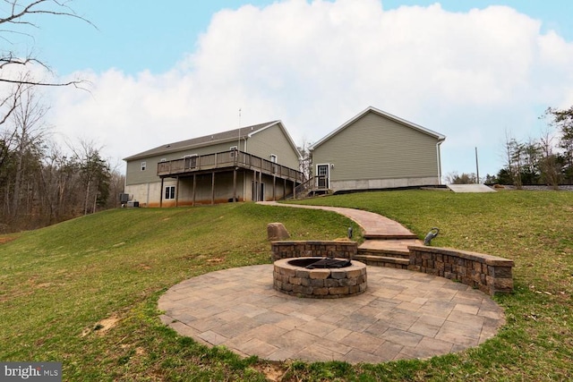 back of property featuring a wooden deck, a patio area, a lawn, and a fire pit