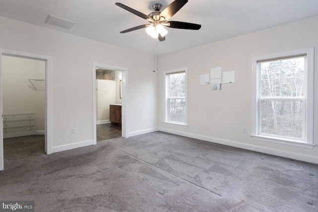 unfurnished bedroom featuring a ceiling fan, baseboards, a spacious closet, ensuite bathroom, and carpet flooring