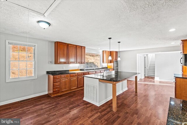 kitchen with a kitchen island, dark hardwood / wood-style floors, pendant lighting, sink, and stainless steel appliances