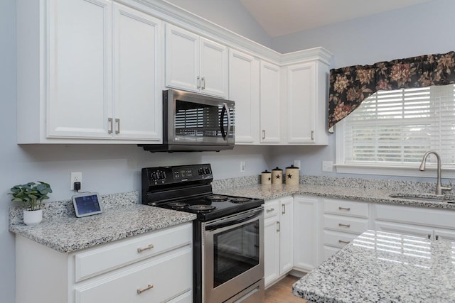 kitchen featuring stainless steel appliances, lofted ceiling, white cabinetry, a sink, and light stone countertops