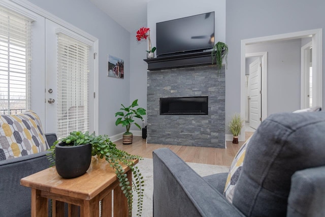 living area featuring french doors, a stone fireplace, baseboards, and wood finished floors