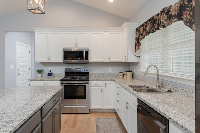 kitchen featuring light wood finished floors, appliances with stainless steel finishes, white cabinets, vaulted ceiling, and a sink