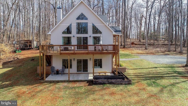 back of property with a patio, a wooden deck, a yard, a shingled roof, and a chimney