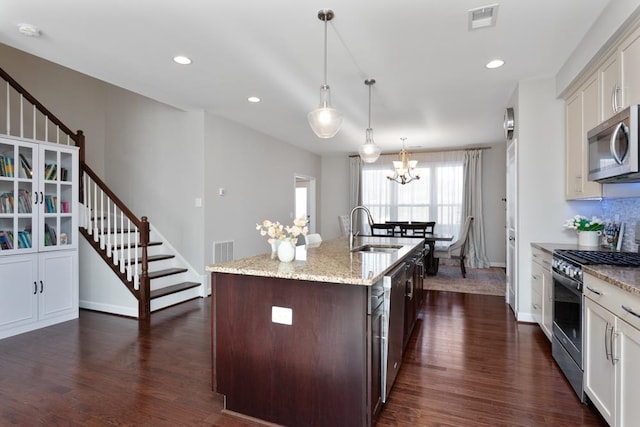 kitchen with appliances with stainless steel finishes, pendant lighting, an island with sink, sink, and light stone counters