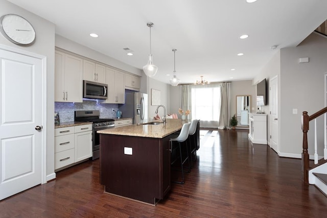 kitchen featuring decorative light fixtures, a breakfast bar area, a kitchen island with sink, stainless steel appliances, and light stone countertops