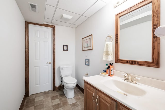 bathroom with visible vents, baseboards, a drop ceiling, toilet, and vanity