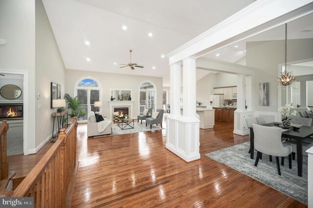 dining room featuring ceiling fan with notable chandelier, high vaulted ceiling, decorative columns, hardwood / wood-style flooring, and crown molding