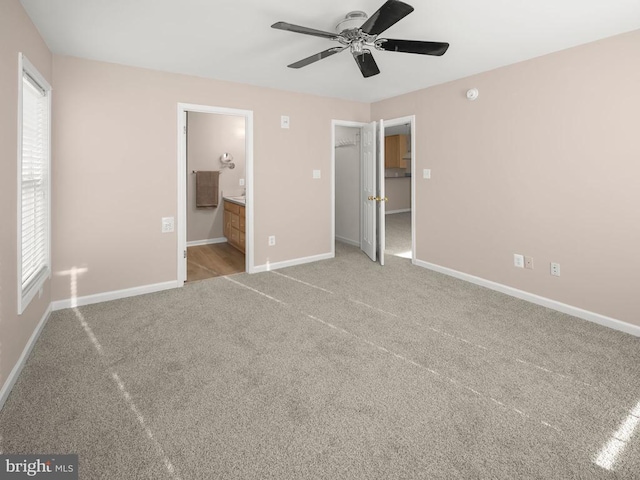 unfurnished bedroom featuring baseboards, ensuite bath, ceiling fan, carpet, and a walk in closet