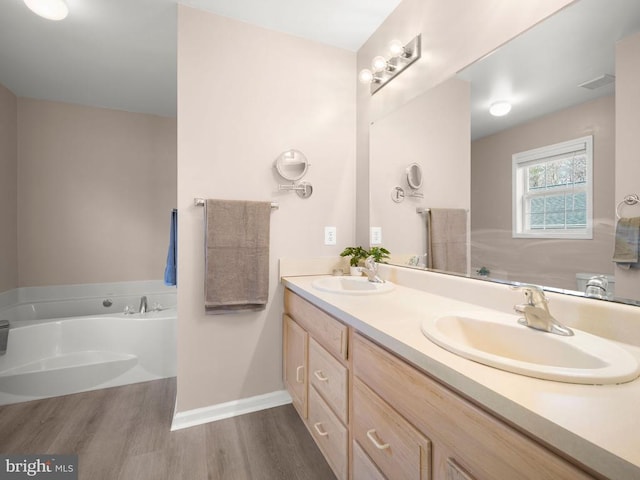 bathroom featuring a garden tub, double vanity, visible vents, a sink, and wood finished floors