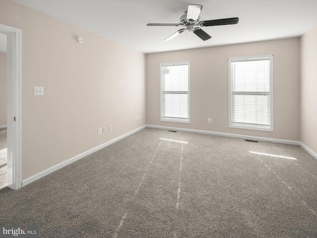 carpeted spare room with visible vents, baseboards, and a ceiling fan