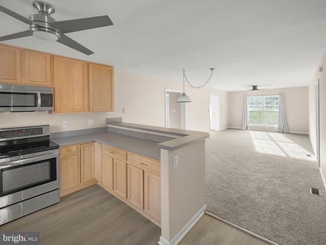 kitchen with appliances with stainless steel finishes, open floor plan, a peninsula, and light brown cabinetry