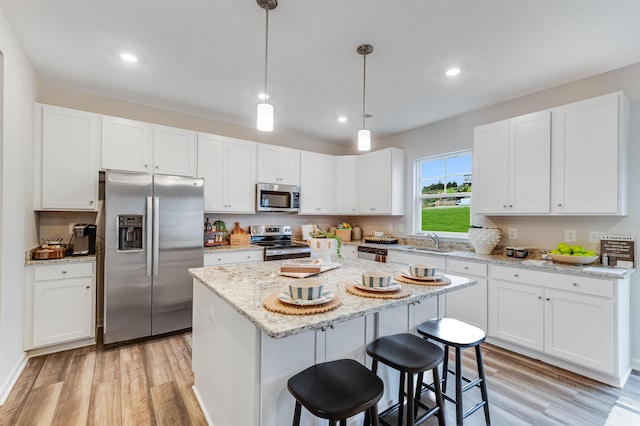 kitchen with appliances with stainless steel finishes, a sink, light wood finished floors, and a center island