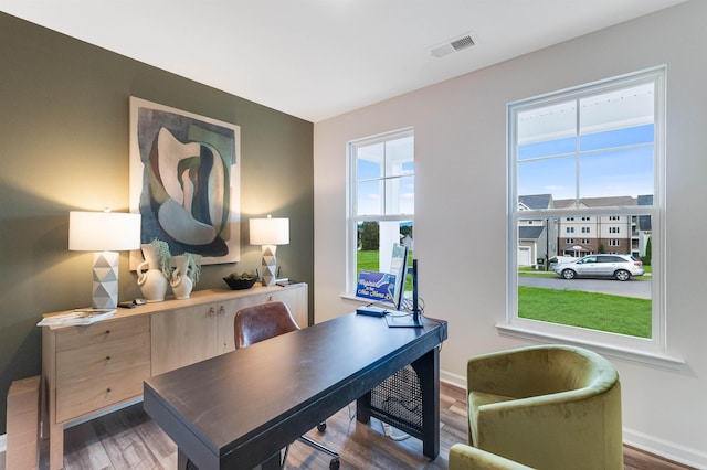 office with visible vents, baseboards, wood finished floors, and a healthy amount of sunlight