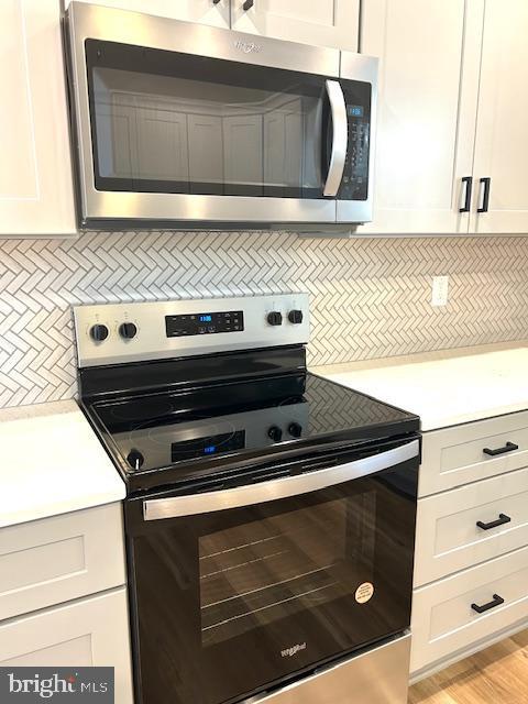 kitchen with white cabinetry, decorative backsplash, light hardwood / wood-style flooring, and appliances with stainless steel finishes