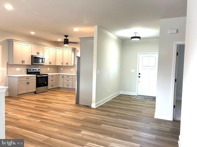 kitchen with backsplash, light hardwood / wood-style flooring, ceiling fan, and appliances with stainless steel finishes