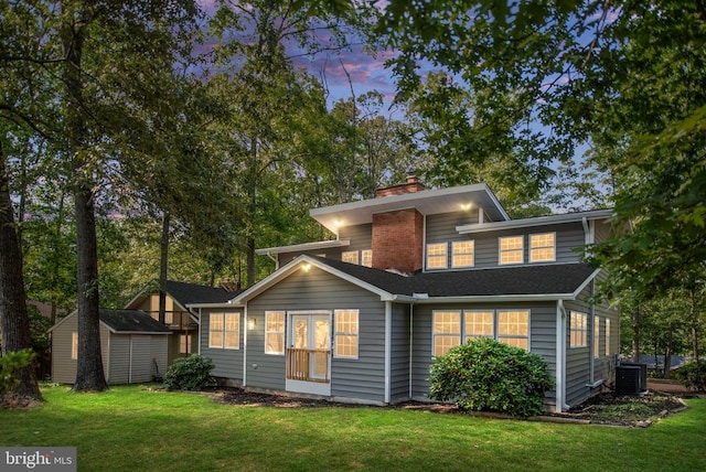 back of house at dusk featuring a lawn, a shed, an outdoor structure, and central air condition unit