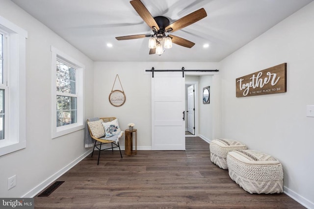 living area featuring visible vents, dark wood finished floors, baseboards, and a barn door