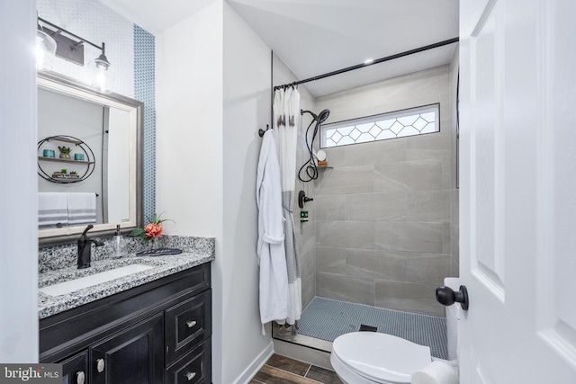 bathroom featuring toilet, wood finished floors, tiled shower, and vanity