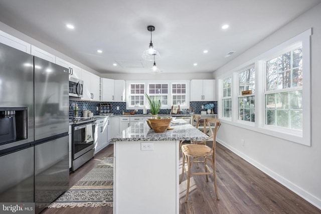 kitchen featuring a kitchen island, white cabinets, a kitchen breakfast bar, appliances with stainless steel finishes, and tasteful backsplash