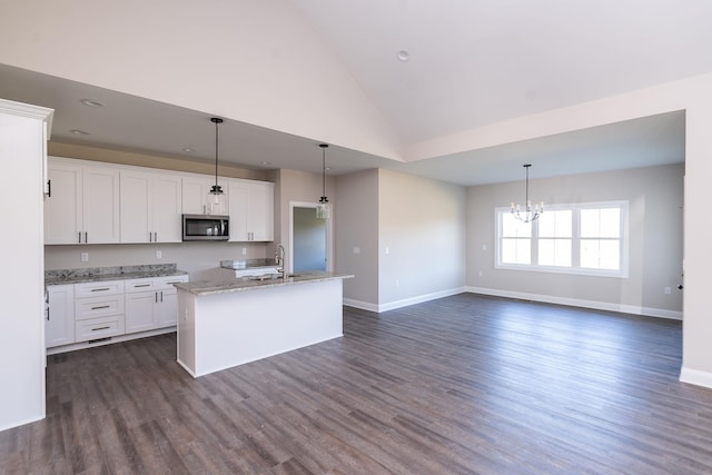 kitchen featuring light stone countertops, an island with sink, hanging light fixtures, and white cabinets