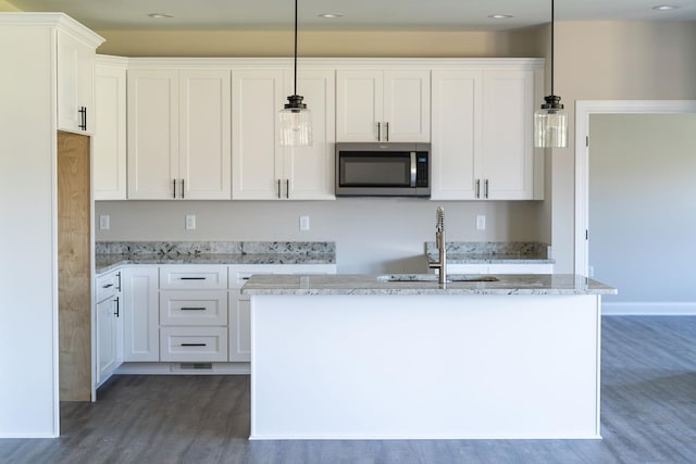 kitchen featuring pendant lighting, white cabinetry, a kitchen island with sink, and light stone countertops