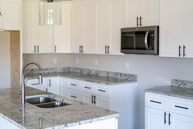 kitchen with white cabinetry, sink, light stone counters, and hanging light fixtures