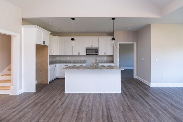 kitchen with decorative light fixtures, white cabinetry, light stone counters, dark wood-type flooring, and a center island with sink