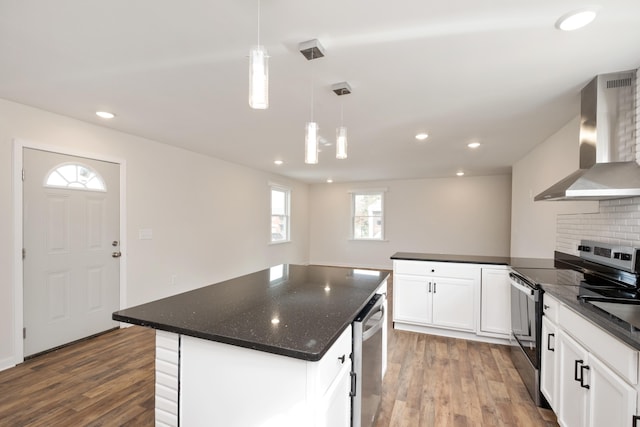 kitchen with appliances with stainless steel finishes, white cabinetry, a center island, decorative light fixtures, and wall chimney exhaust hood