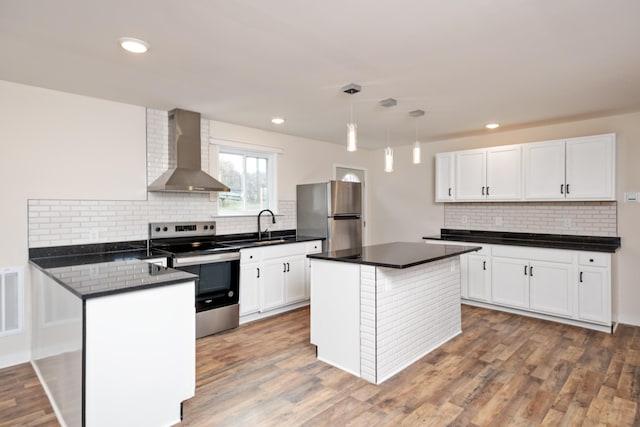 kitchen featuring appliances with stainless steel finishes, white cabinets, hanging light fixtures, hardwood / wood-style flooring, and wall chimney range hood