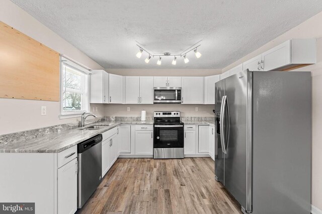 kitchen with appliances with stainless steel finishes, sink, white cabinets, a textured ceiling, and light hardwood / wood-style flooring