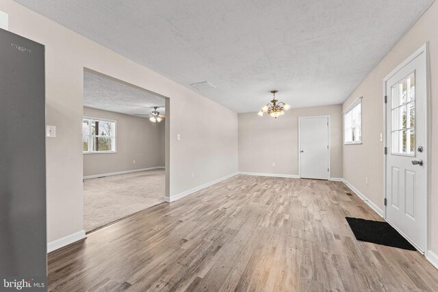 entryway with ceiling fan with notable chandelier, light hardwood / wood-style flooring, and a textured ceiling