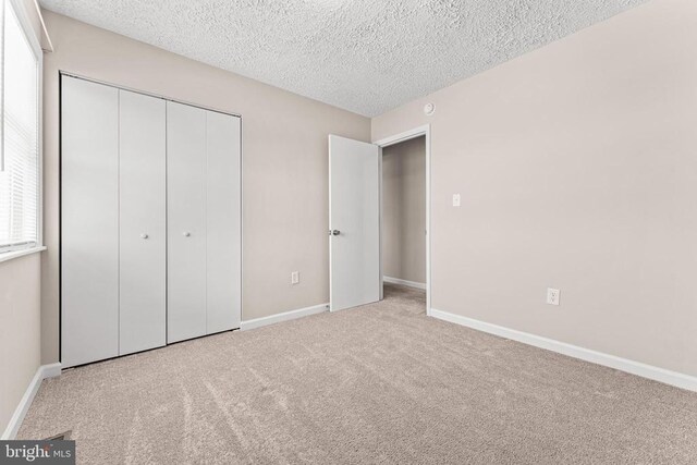 unfurnished bedroom with light carpet, a closet, and a textured ceiling