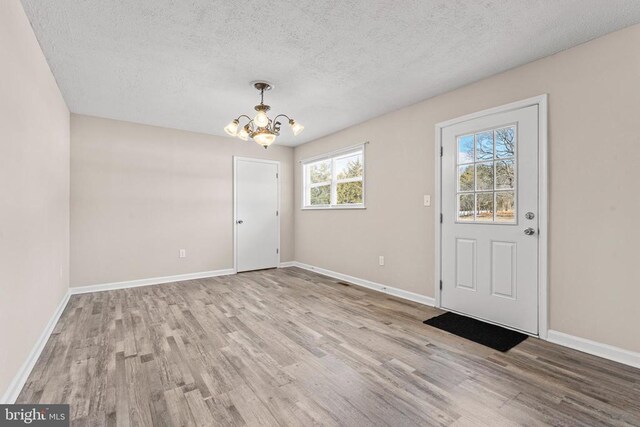 entryway with a textured ceiling, a chandelier, and light hardwood / wood-style flooring