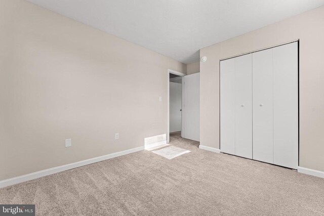 unfurnished bedroom with light colored carpet and a closet