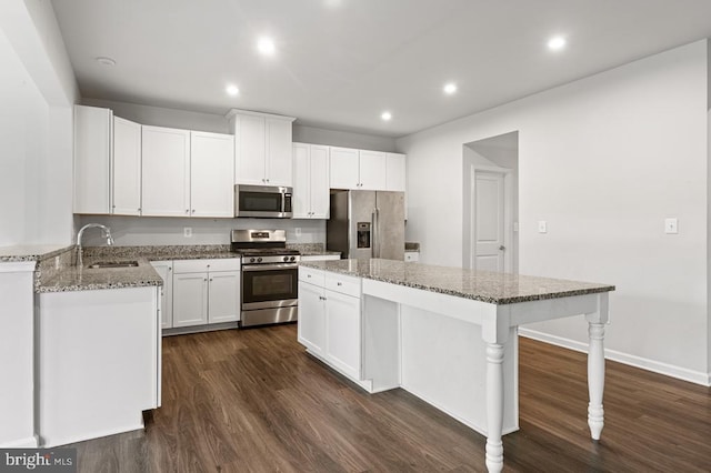 kitchen with appliances with stainless steel finishes, sink, white cabinets, light stone counters, and dark wood-type flooring