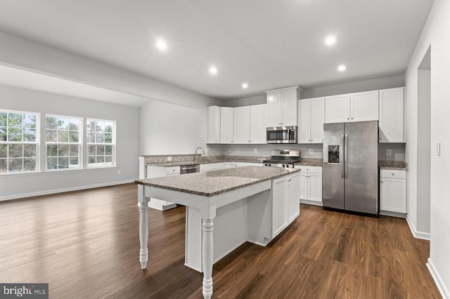 kitchen featuring a kitchen island, appliances with stainless steel finishes, white cabinetry, a breakfast bar area, and light stone counters