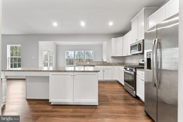 kitchen with stainless steel appliances, white cabinetry, light stone countertops, and a center island