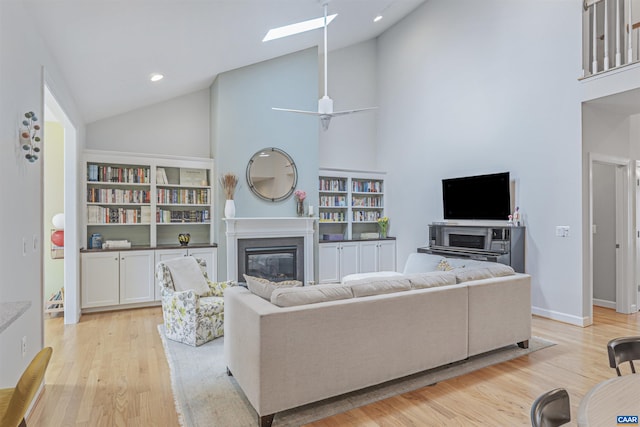 living room with high vaulted ceiling, a glass covered fireplace, recessed lighting, light wood-type flooring, and a skylight