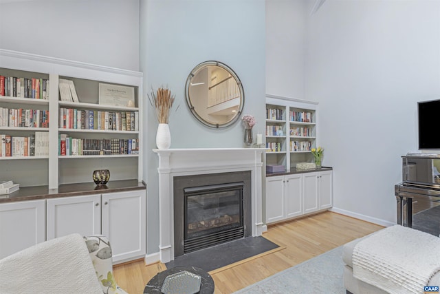 living room with baseboards, a fireplace with flush hearth, and light wood finished floors