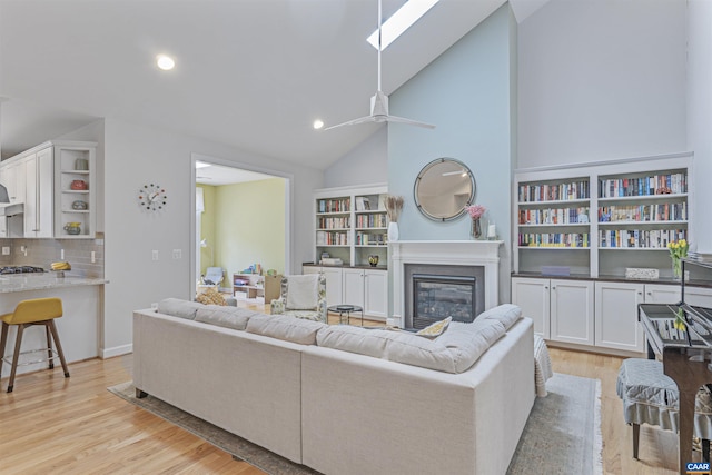 living area featuring light wood-style floors, a skylight, high vaulted ceiling, a glass covered fireplace, and recessed lighting