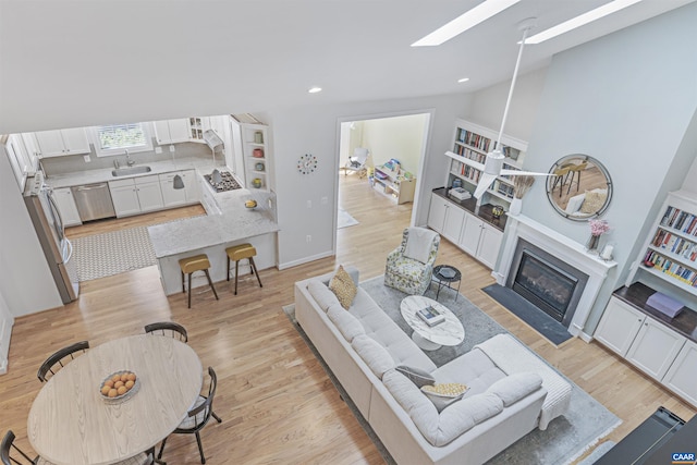 living area with recessed lighting, a skylight, a fireplace with flush hearth, and light wood-style floors