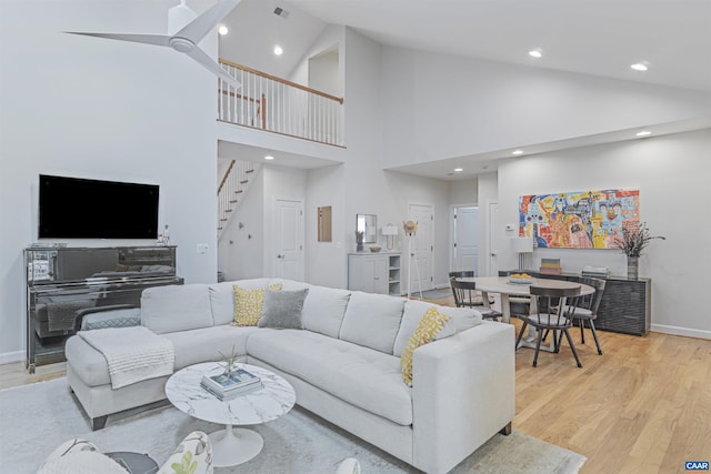 living room with stairway, high vaulted ceiling, baseboards, recessed lighting, and light wood-style flooring
