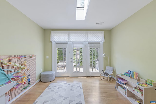 playroom with a skylight, baseboards, wood finished floors, and visible vents