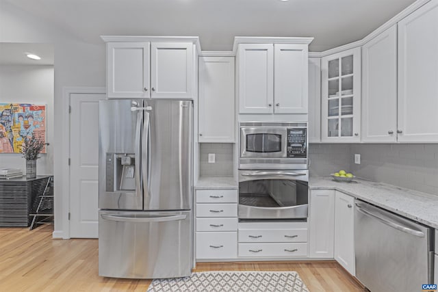 kitchen featuring white cabinets, light stone countertops, light wood-style flooring, stainless steel appliances, and glass insert cabinets