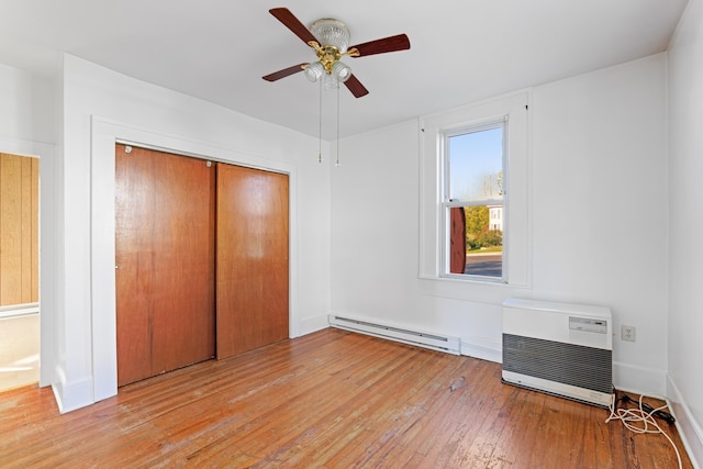 unfurnished bedroom featuring a wall mounted AC, light wood-type flooring, baseboard heating, a closet, and ceiling fan