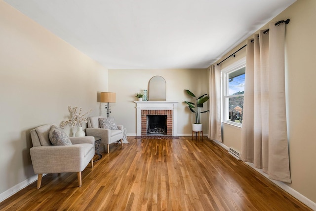 sitting room featuring visible vents, a brick fireplace, baseboards, and wood finished floors