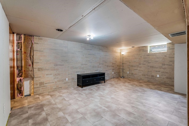 basement featuring visible vents and brick wall