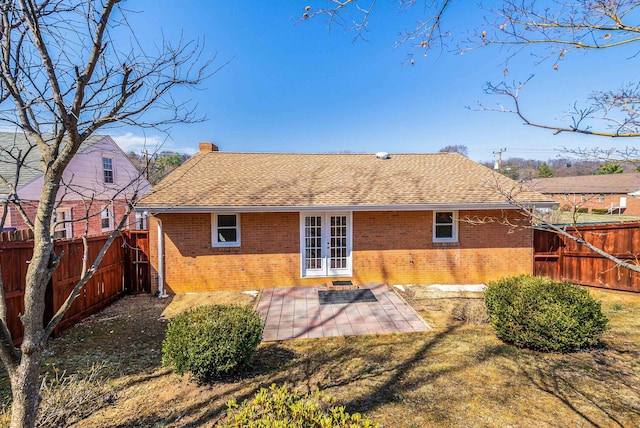 back of house with roof with shingles, a fenced backyard, french doors, a patio area, and brick siding