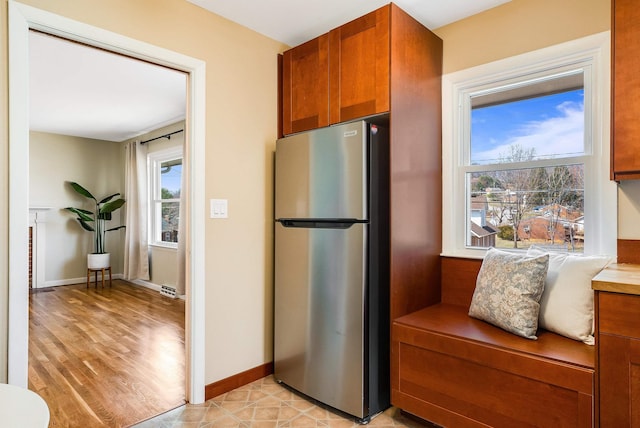 kitchen with light wood-type flooring, freestanding refrigerator, brown cabinetry, light countertops, and baseboards